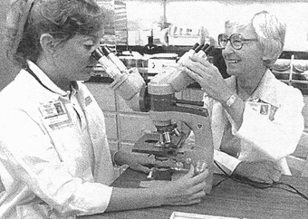 Ruth Morris smiles at student looking through a microscope.