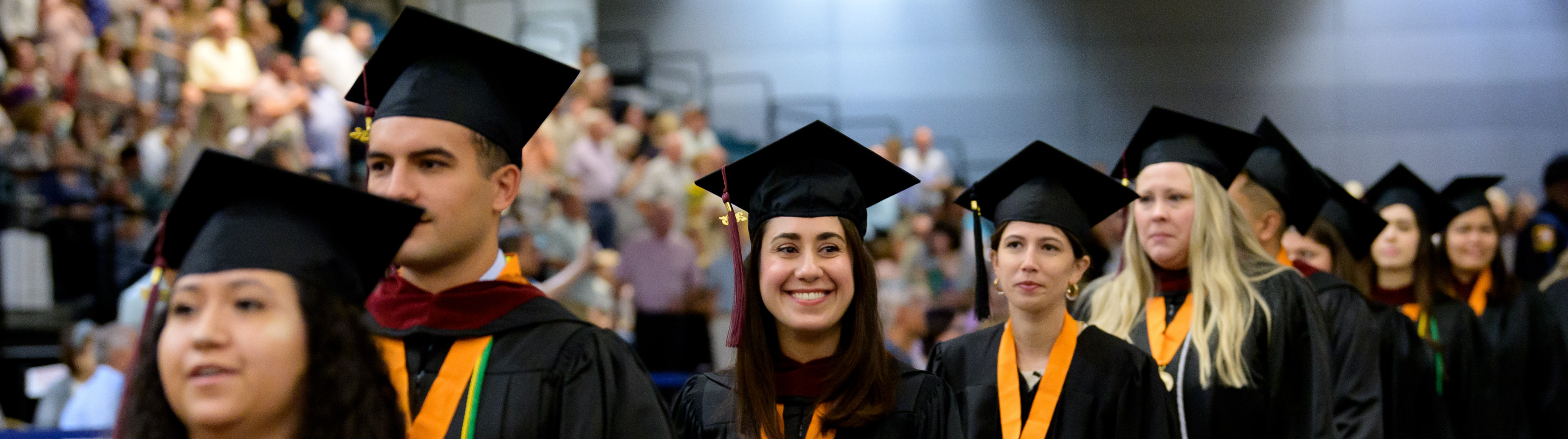 Graduates walking and smiling to family and friends in the stands