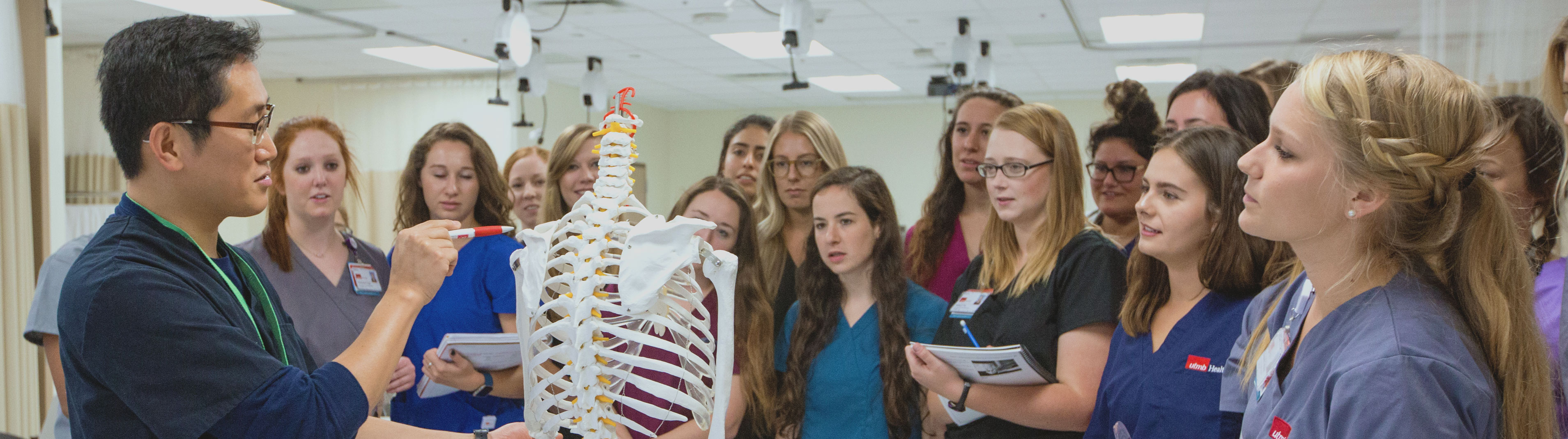 Professor points to the clavicle bone on a skeleton in front of several students.