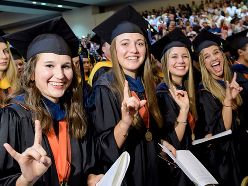 Four students excitedly pose using the University of Texas Hook Em Horns hand sign.