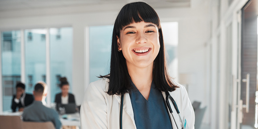 A healthcare professional wearing a white coat holds a clipboard in a bright clinical setting.